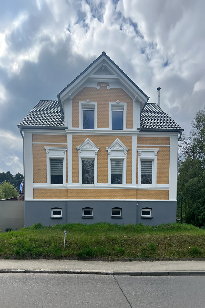 Frontansicht eines historischen Privatwohnhauses mit sanierter Klinkerfassade, weißen Zierelementen, Fensterumrahmungen und grauem Sockelbereich nach fachgerechter Fassadensanierung.