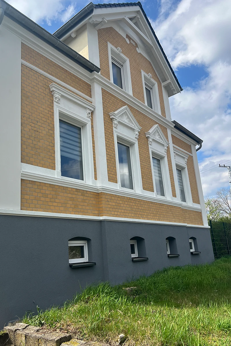 Historisches Privatwohnhaus mit sanierter Klinkerfassade, weißen Zierelementen, Fensterrahmungen und grauem Sockelbereich nach fachgerechter Fassadensanierung.