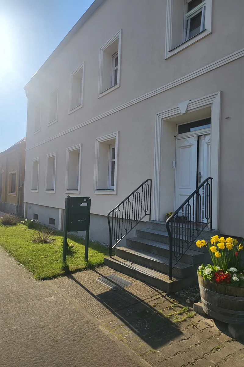 Eingangsbereich eines Bürogebäudes mit heller Fassade, dekorativen Bossenelementen, weißen Fensterrahmungen und Treppe nach hochwertigen Fassadenarbeiten mit WDVS.