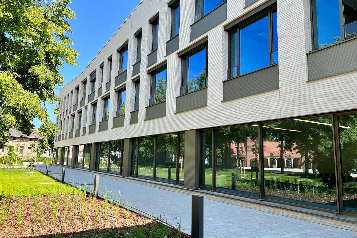 Modernes Verwaltungsgebäude mit heller Klinkerriemchen-Fassade, großen Glasflächen und begrüntem Außenbereich als Beispiel für hochwertige Fassadengestaltung und Fassadensanierung.