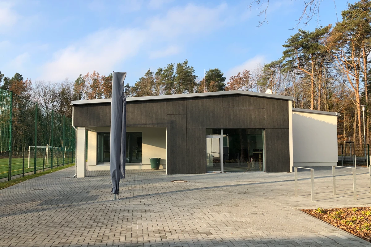 Funktionsgebäude am Sportplatz Michendorf mit dunkler VHF-Fassadenbekleidung, heller Fassade und großen Glasflächen nach professioneller Fassadensanierung mit WDVS.