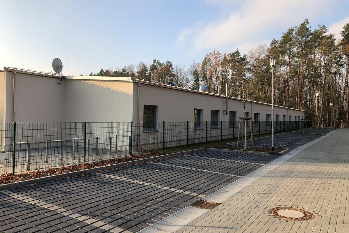 Langes Funktionsgebäude am Sportplatz Michendorf mit heller Fassade, Zaunanlage und gepflastertem Außenbereich nach Fassadensanierung mit WDVS.