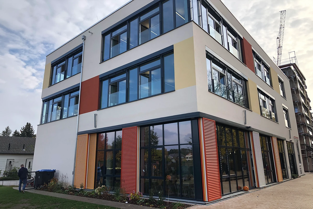 Modernisierte Schulfassade mit großen Glasflächen, farbigen Fassadenelementen und Sonnenschutzlamellen nach professioneller Fassadensanierung mit WDVS.