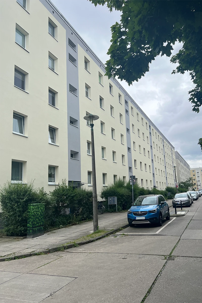 Langes Mehrfamilienhaus mit heller Fassade, grauem Akzentstreifen und Straßenansicht nach professioneller Fassadenbeschichtung und Anstricharbeiten.