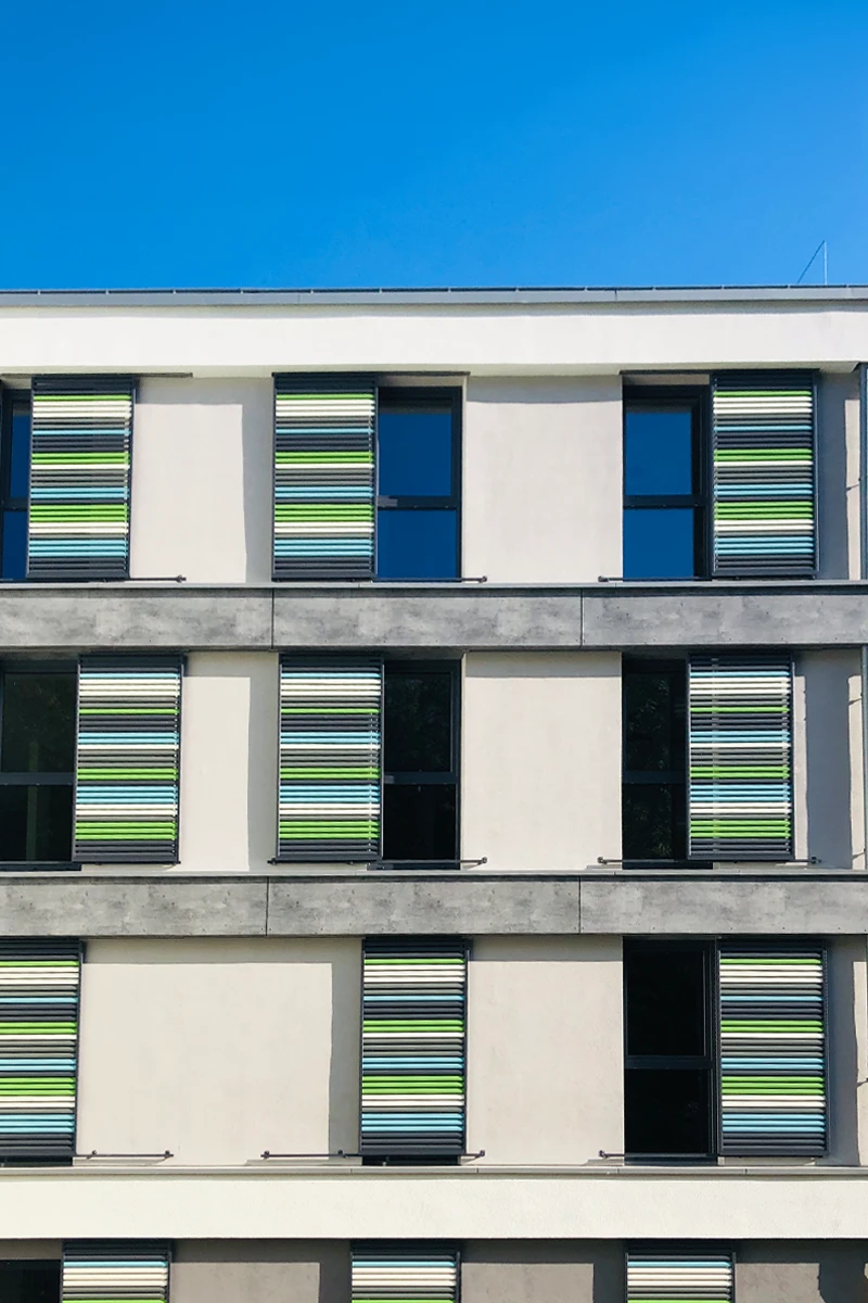 Fassade eines Studentenwohnheims mit moderner Fassadengestaltung, großen Fenstern und farbigen Sonnenschutzelementen als Teil einer professionellen Fassadensanierung.