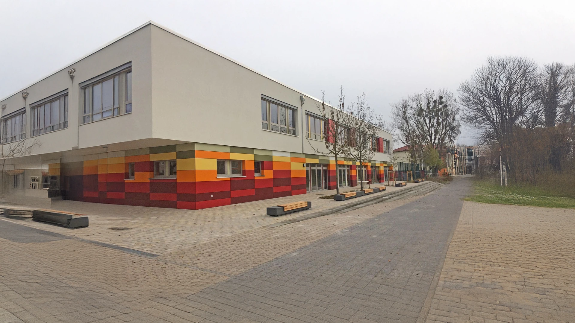 Modernisierte Kita mit farbiger Fassade nach Fassadensanierung, großem Vorplatz und saniertem Gebäude im Außenbereich.
